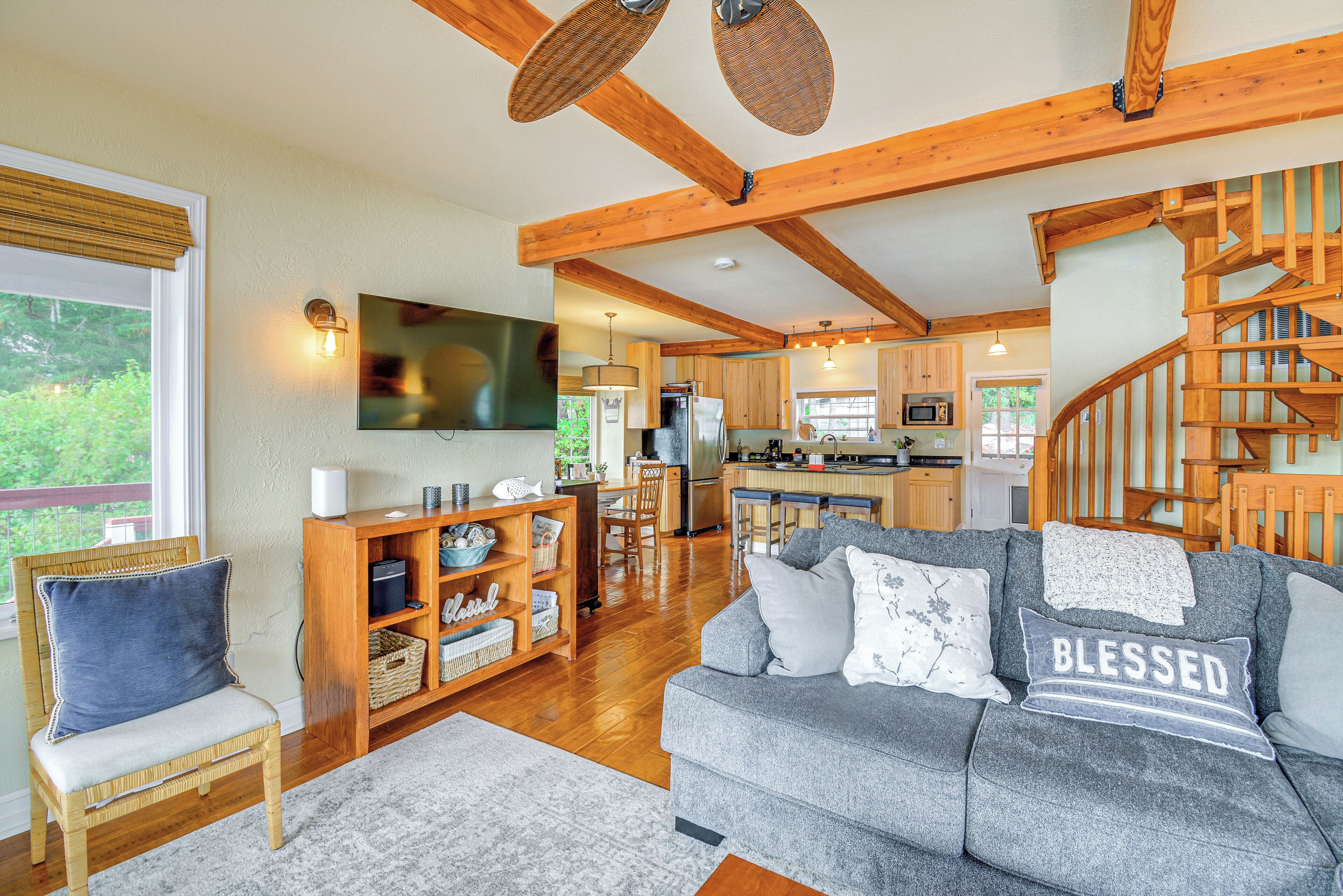 A spacious living room with a grey sofa, wooden beams, a wooden chair, and a staircase.