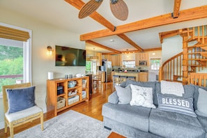A spacious living room with a grey sofa, wooden beams, a wooden chair, and a staircase.