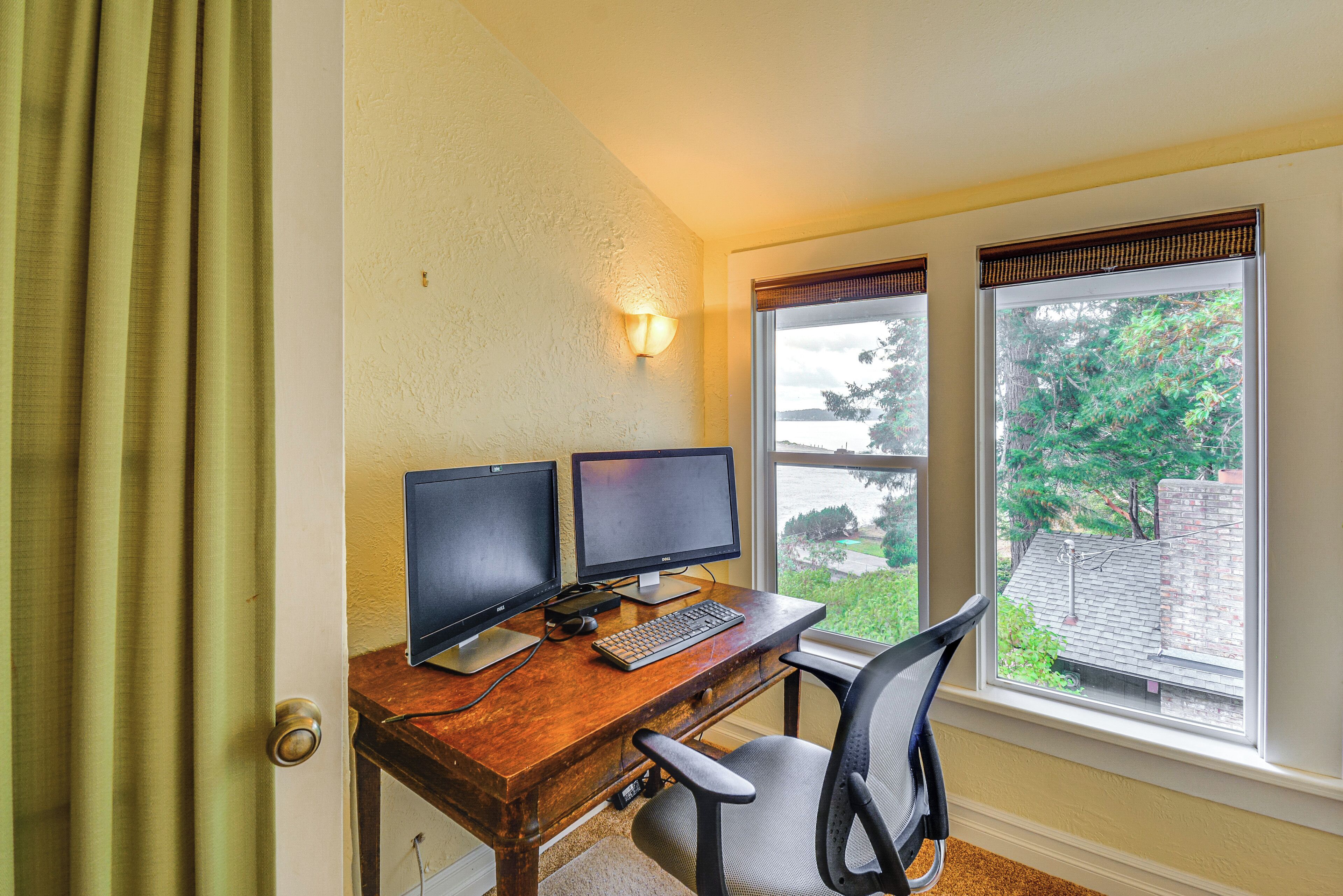 A room with a wooden desk, two monitors, a keyboard, and a chair.