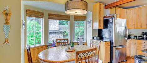 A kitchen with wooden cabinets, a stainless steel refrigerator, a dining table with chairs, and a hanging light fixture.