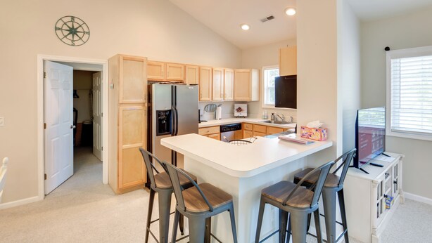 A modern kitchen with wooden cabinets, a central island with bar stools, a refrigerator, a dishwasher, and a TV. - 4 Mi to Beach: Lewes Townhome w/ Ping-pong Table (Rehoboth Beach)
