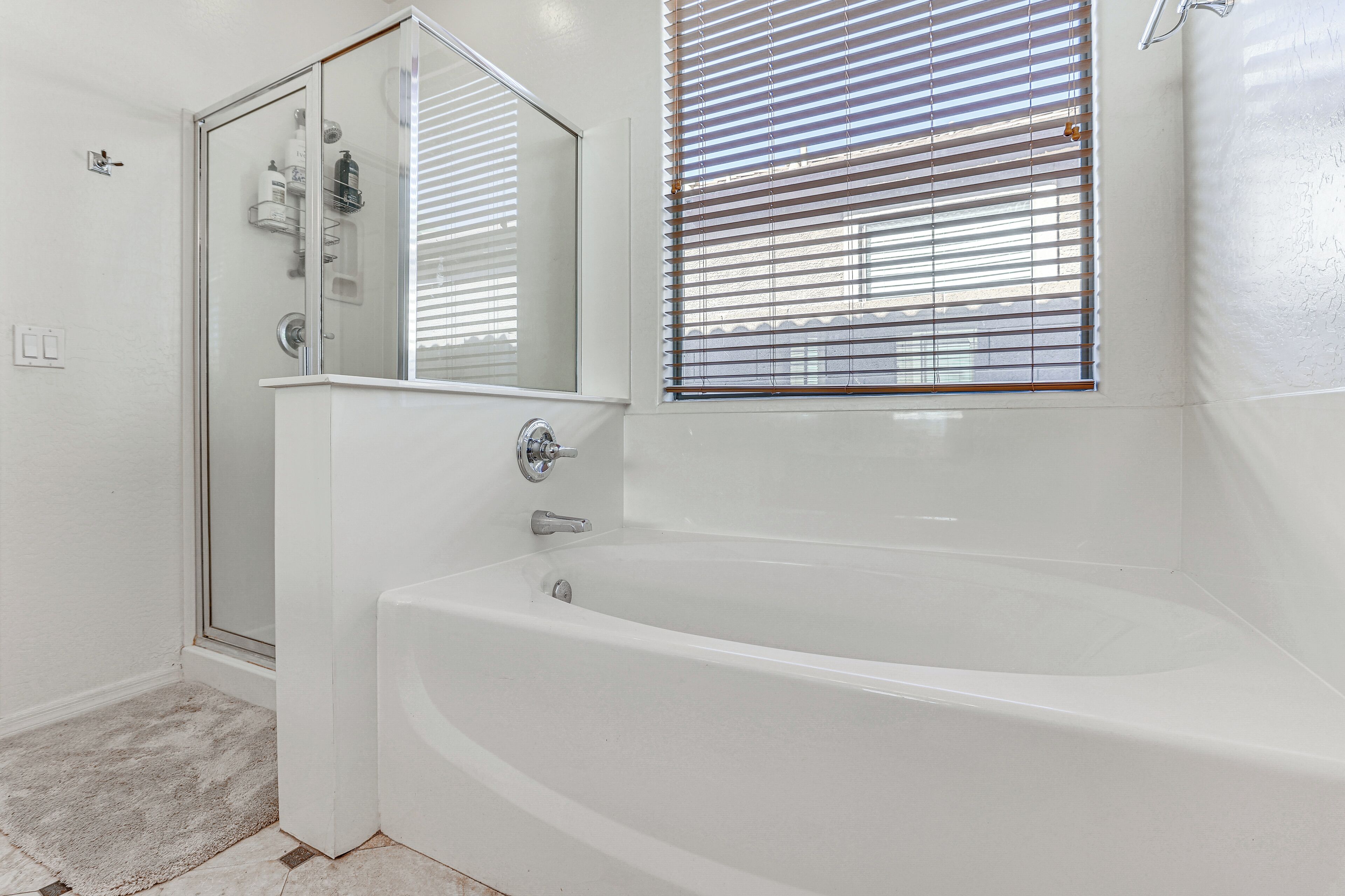 Ein Badezimmer mit einer Glasdusche, einer Badewanne und einem Fenster mit Jalousien.