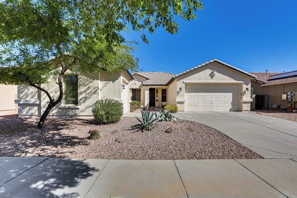 A residential house with a garage, a driveway, and a landscaped garden with a tree and a cactus.