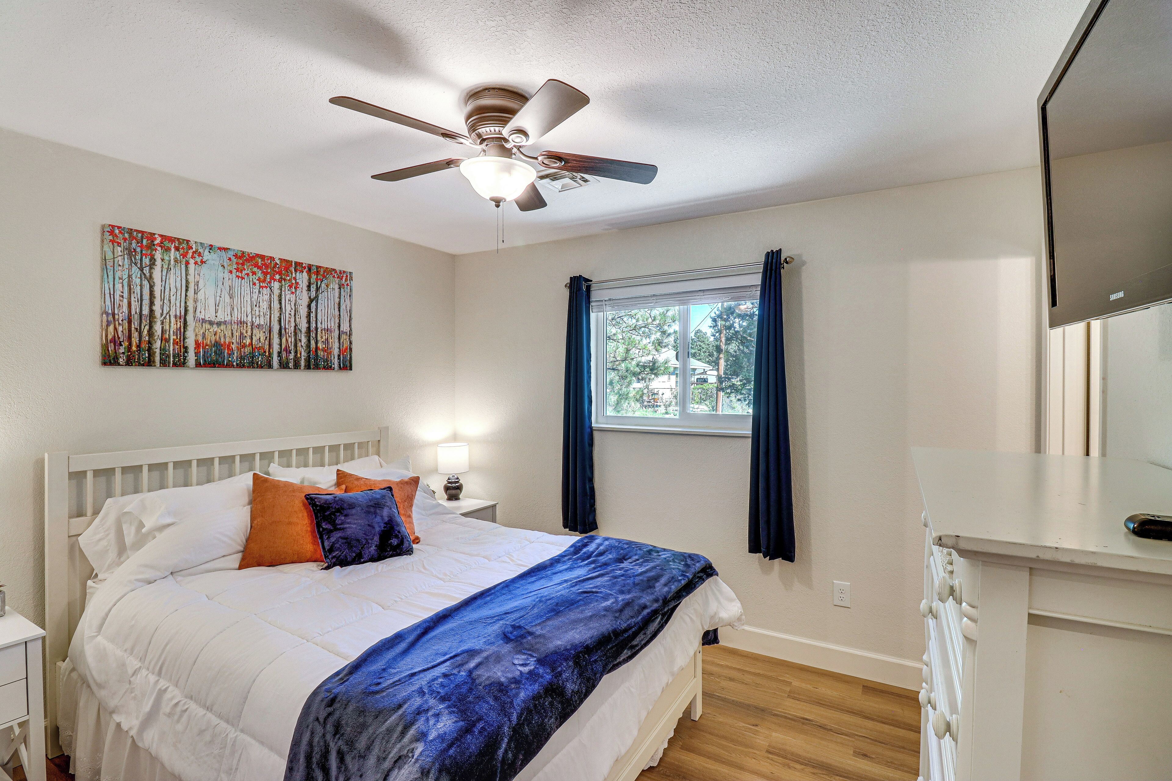 A bedroom with a bed, a ceiling fan, a window with curtains, and a painting on the wall.