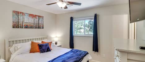 A bedroom with a bed, a ceiling fan, a window with curtains, and a painting on the wall.