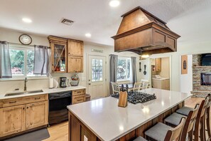 A modern kitchen with wooden cabinets, a large island, and a stone fireplace. - Near Woodland Lake Park: Home w/ Fire Pit! (Lakeside)