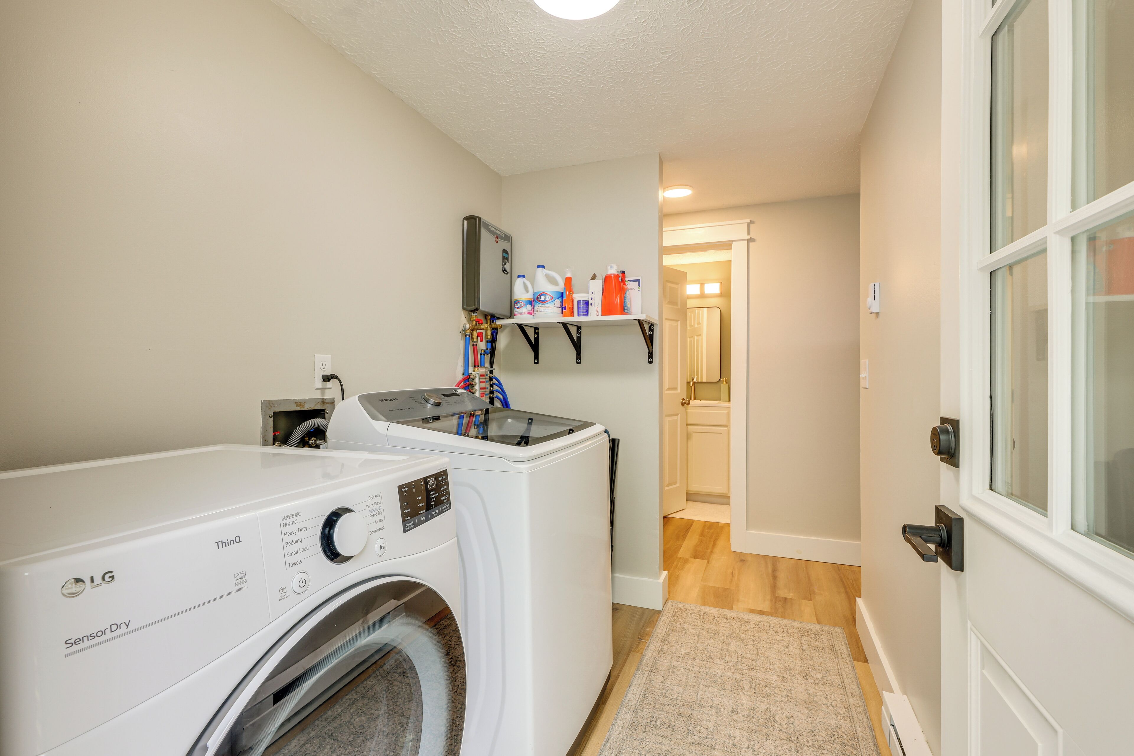 A laundry room with two washing machines, a shelf with cleaning supplies, and a door leading to another room.