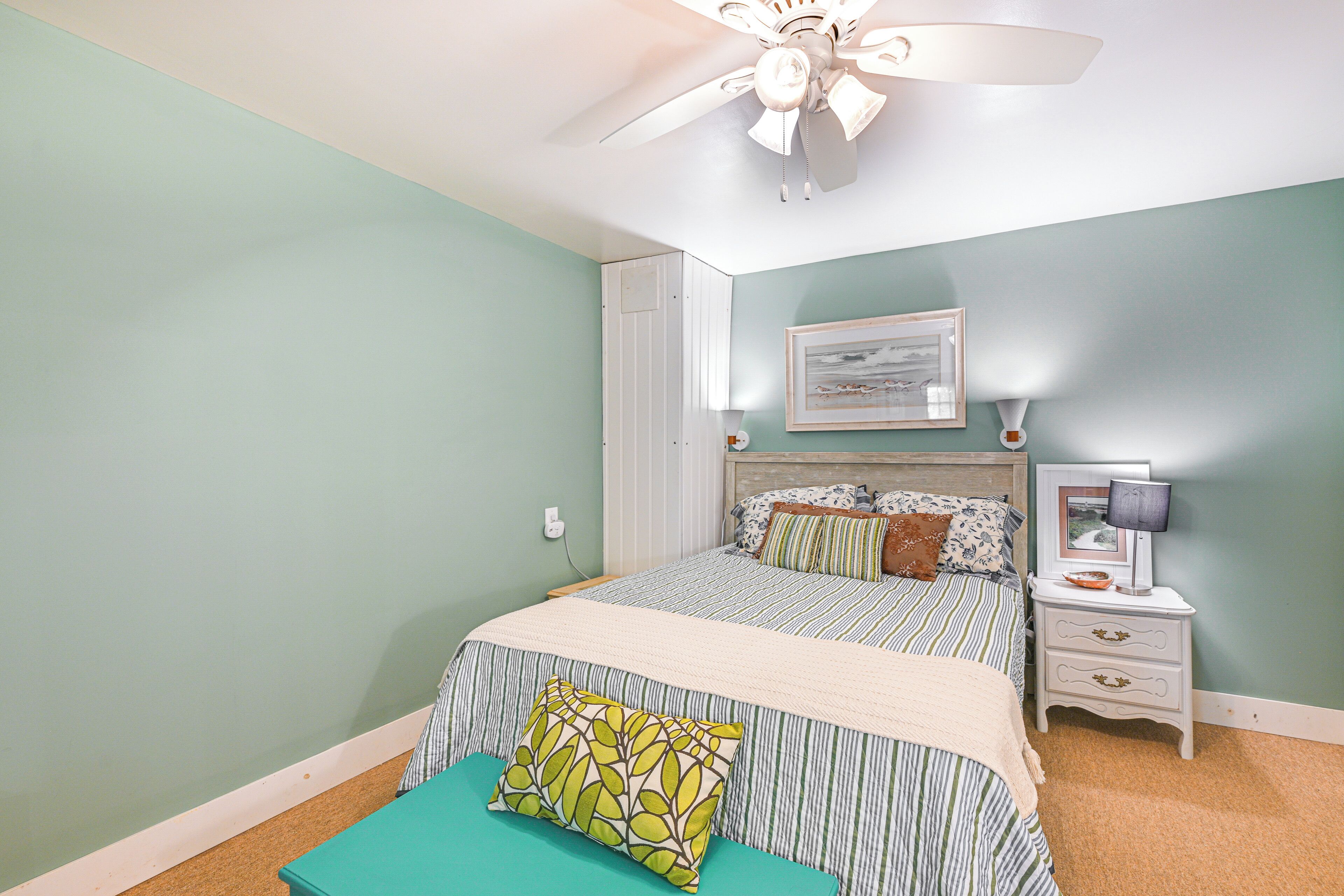A bedroom with a bed, a nightstand, a ceiling fan, and a wall-mounted picture.