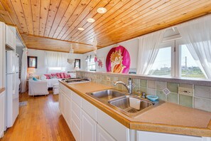 Cocina con techo de madera, armarios blancos, un fregadero y una ventana con cortinas.