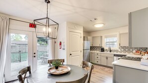 Una cocina moderna con comedor, que incluye una mesa redonda, sillas, una araña y vista al patio trasero a través de puertas de vidrio.