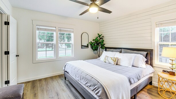 Un dormitorio con cama, ventilador de techo, ventana y planta.