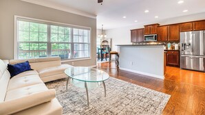 A modern living room with a glass coffee table, beige sofa, and a large window. - 3 Mi to Avalon: Townhome w/ Balcony in Alpharetta! (Milton)