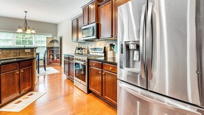 A modern kitchen with stainless steel appliances, wooden cabinets, and a large window providing natural light. - 3 Mi to Avalon: Townhome w/ Balcony in Alpharetta! (Milton)