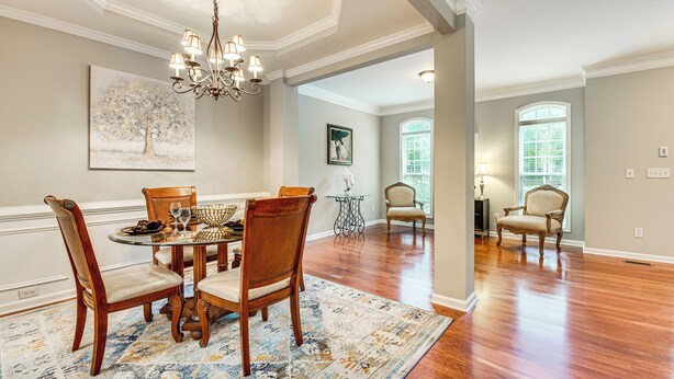 A dining area with a round table, chairs, and a chandelier. There is a window with a view of greenery outside. - 3 Mi to Avalon: Townhome w/ Balcony in Alpharetta! (Milton)