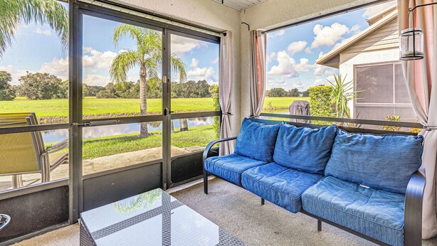 Un patio techado con un sofá azul, una mesa de vidrio y vistas a un paisaje verde a través de amplias puertas correderas.