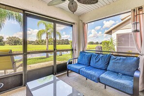 Eine überdachte Terrasse mit einem blauen Sofa, einem Glastisch und Blick auf eine grüne Landschaft durch große Schiebetüren.