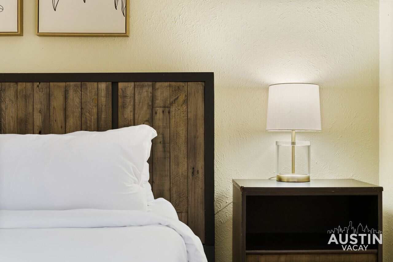 A bed with white linens, a wooden headboard, and a bedside table with a lamp.