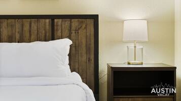 A bed with white linens, a wooden headboard, and a bedside table with a lamp.