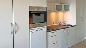 Una cocina moderna con armarios blancos, horno de acero inoxidable, un lavamanos y lavavajillas.
