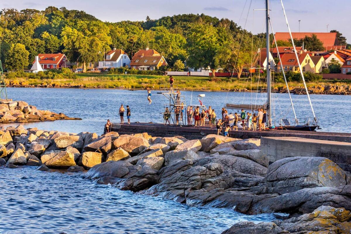 A rocky waterfront with a dock, sailboat, and people engaging in water activities.