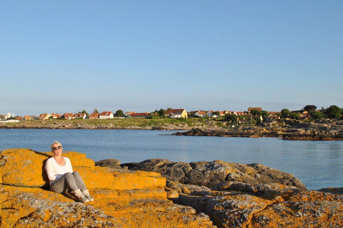A person sitting on rocks by a body of water with houses in the background.
