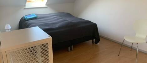 A small, tidy room with a bed, a desk, a chair, and a window.