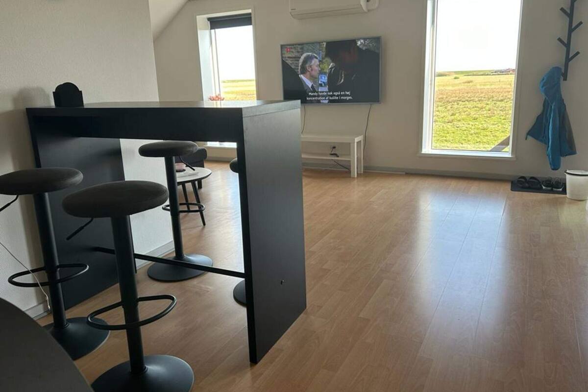 Un espace bar moderne avec des tabourets, un téléviseur et de grandes fenêtres donnant sur l’extérieur.