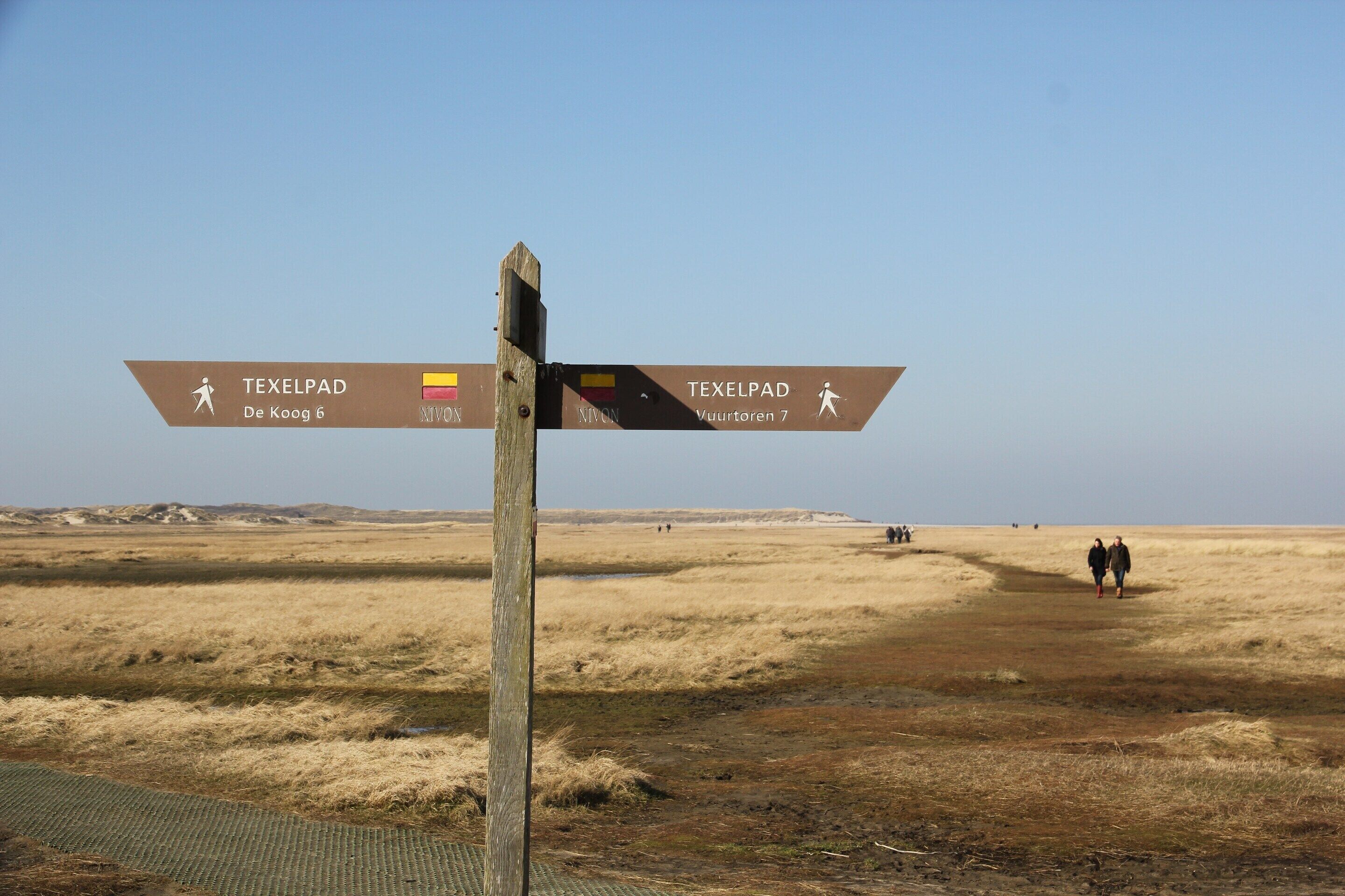Placa de sinalização indicando duas direções em uma paisagem plana.