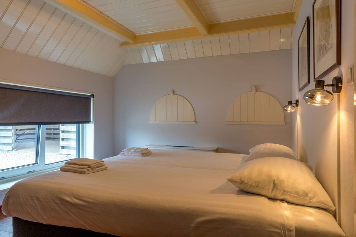 A hotel room with two beds, a large window, and a ceiling with wooden beams.