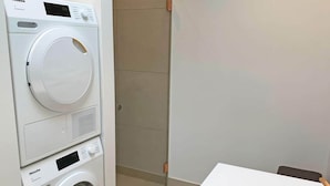 A compact laundry area with a front-loading washing machine and dryer, a white sink with a copper faucet, and a tiled floor. - 6 Person Holiday Home in Svaneke (Svaneke)