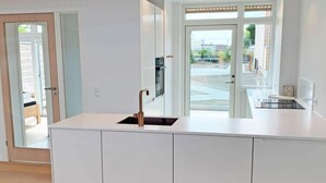 A modern kitchen with a white countertop, a copper faucet, and a view of the outside through a glass door. - 6 Person Holiday Home in Svaneke (Svaneke)