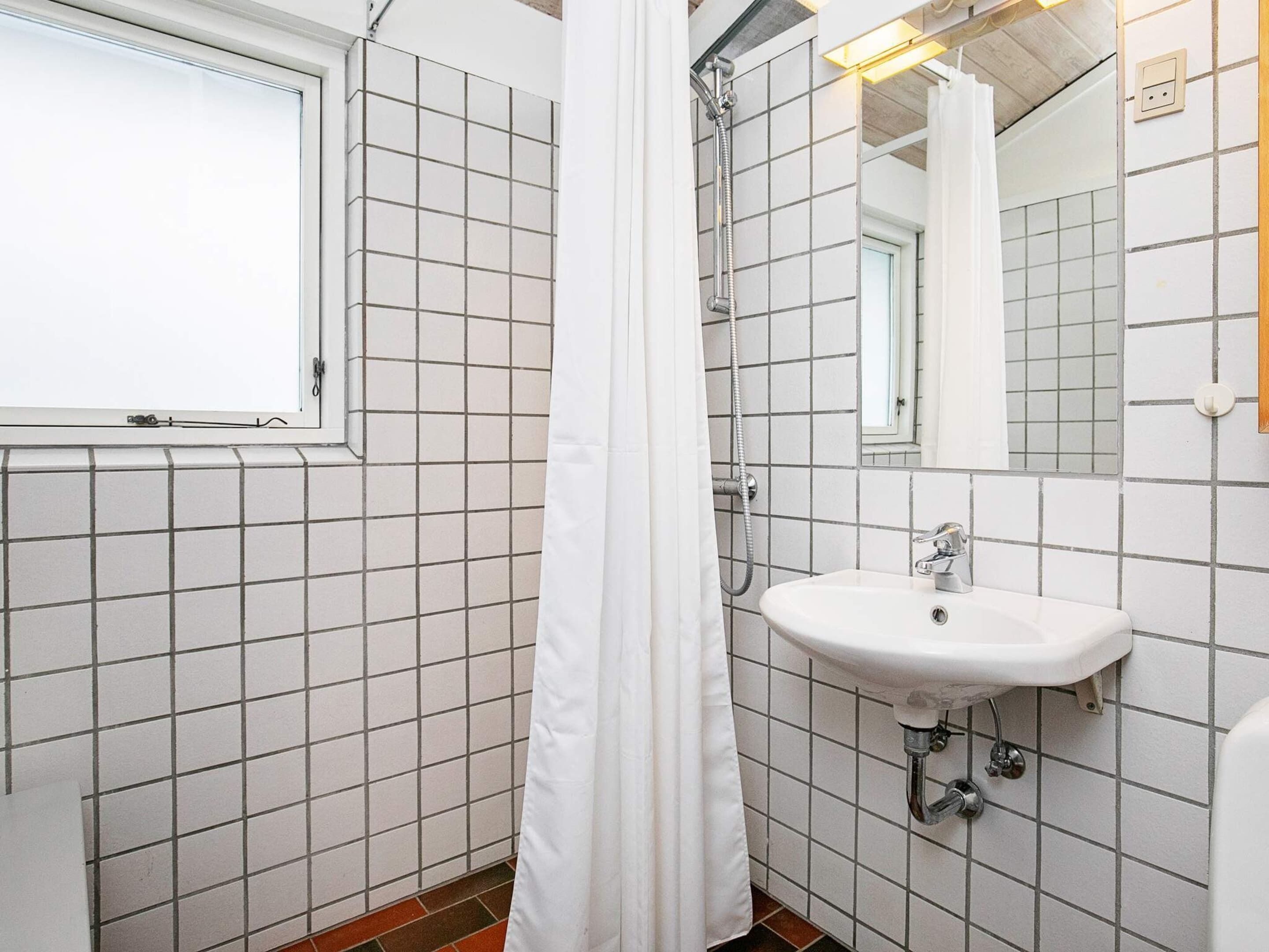 A bathroom with white tiled walls, a window, a sink, and a shower.