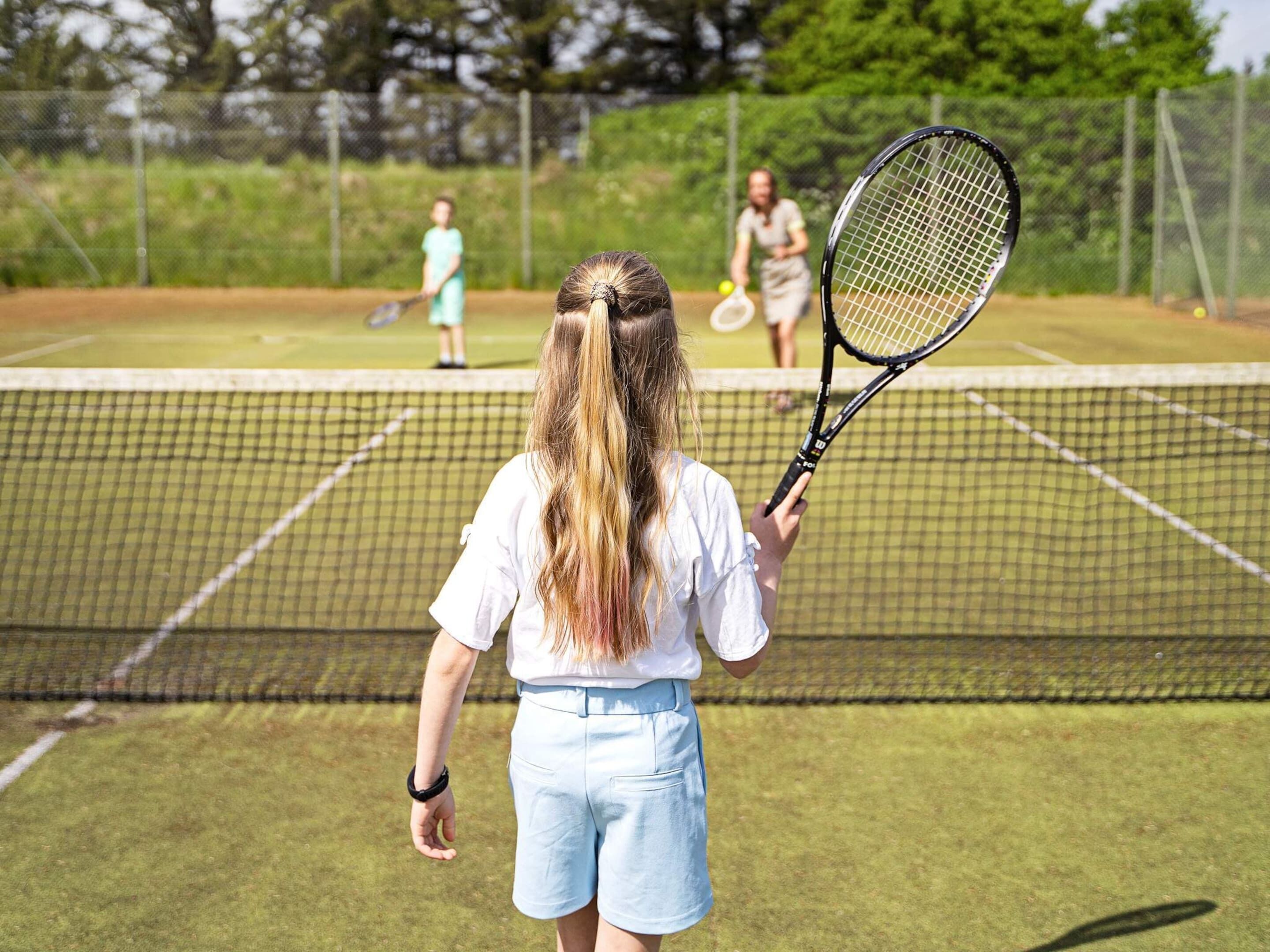 A tennis court with a net in the center, surrounded by a fence.
