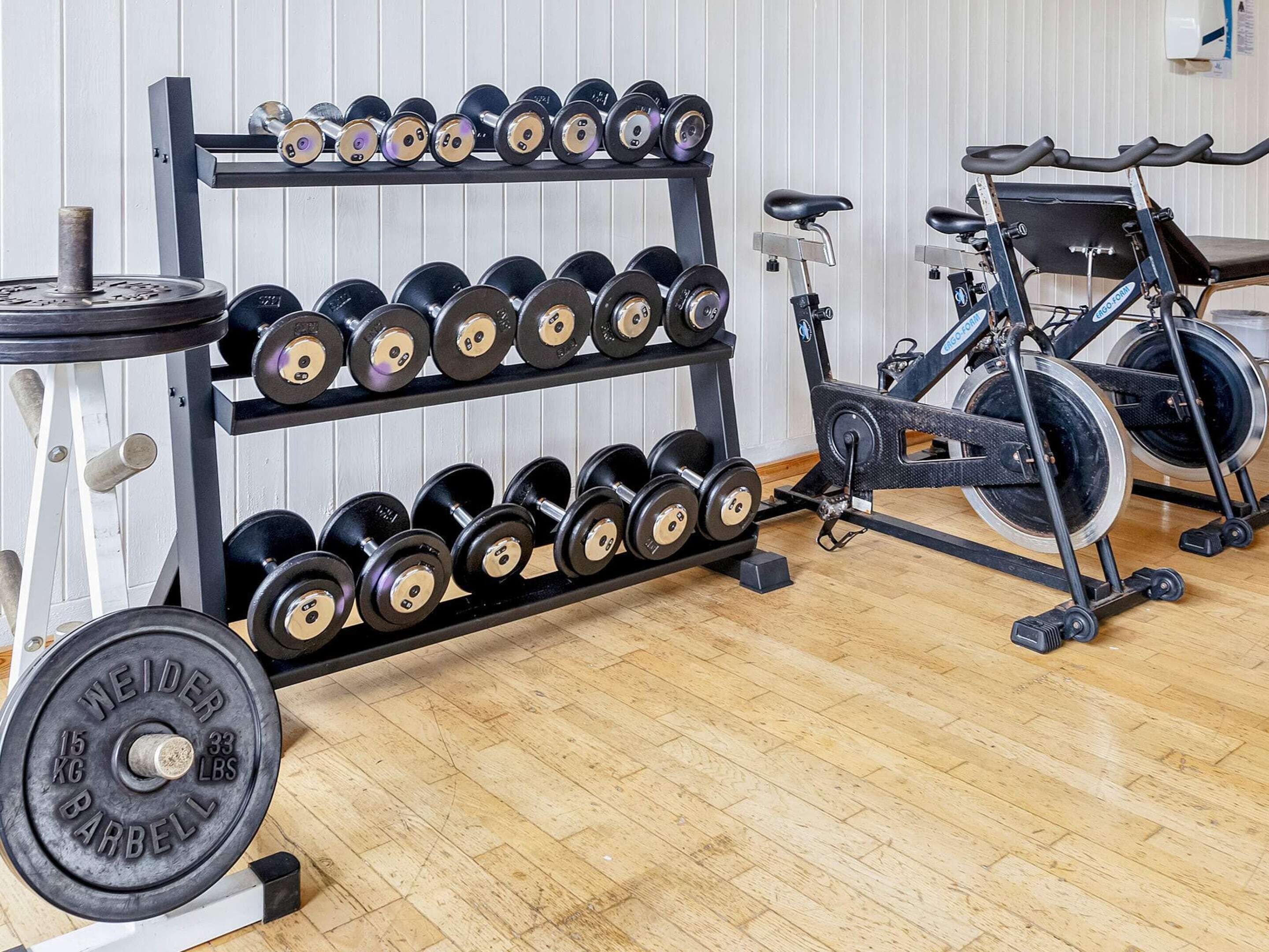 Ein Fitnessstudio mit einem mehrstufigen Hantelständer, einem Ergometer und einer Langhantel.