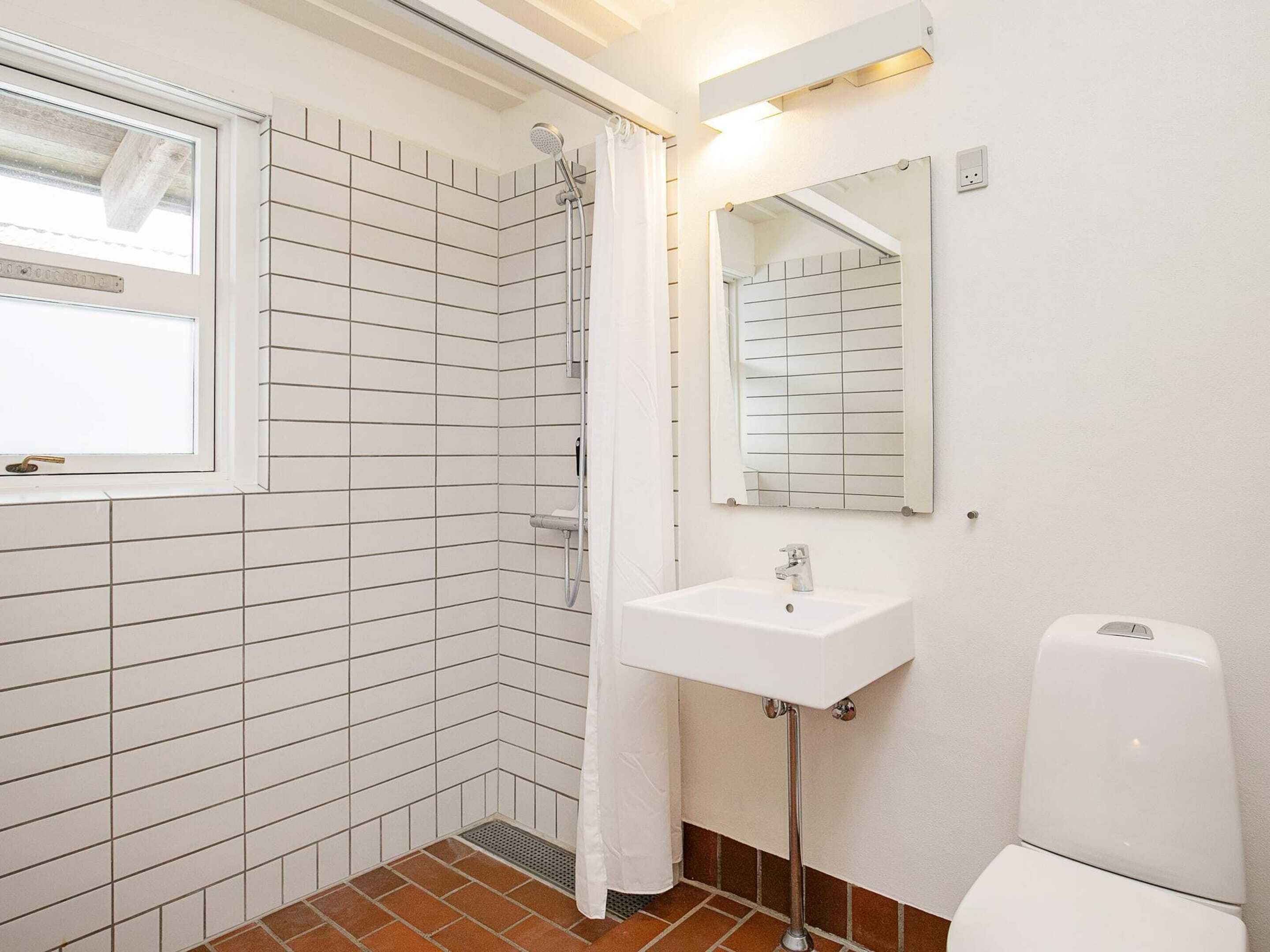 A bathroom with white tiled walls, a shower with a glass door, a white sink, a mirror, and a toilet.