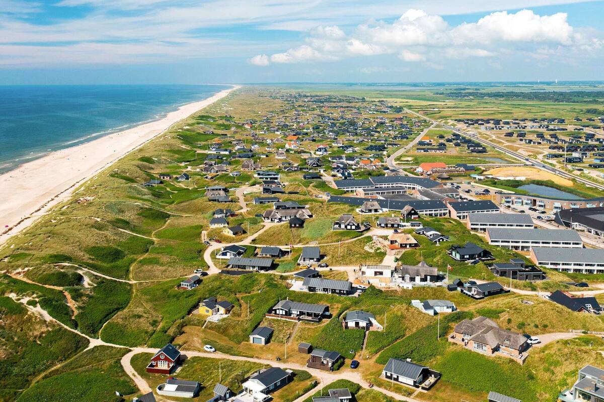 An aerial view of a coastal residential area with houses, a beach, and a road.