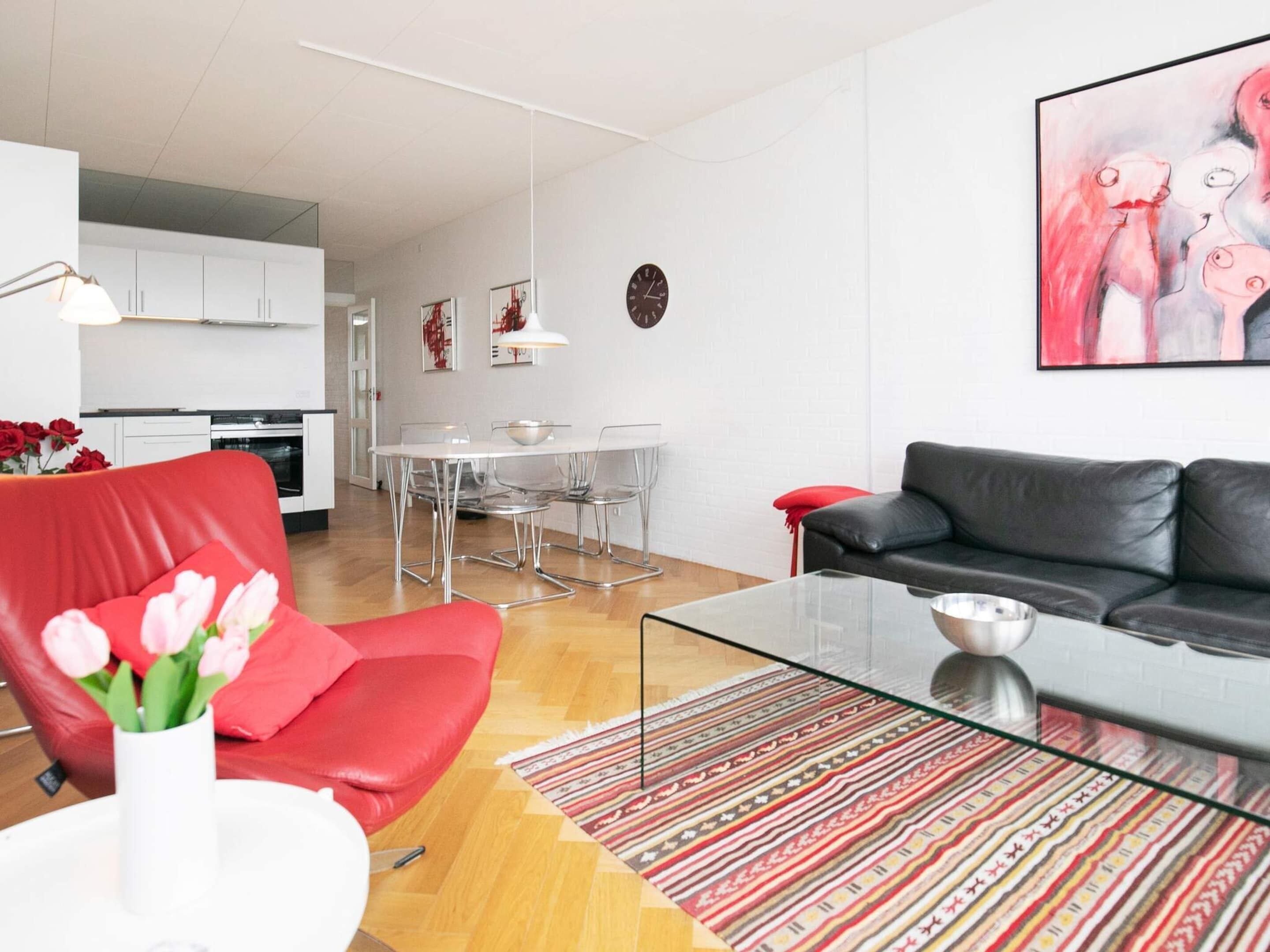 A modern living room with a red sofa, a glass coffee table, and a striped rug.