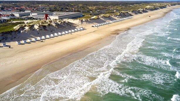 Ein Küstenhotel mit langer Strandpromenade, Sandstrand und Wellen.