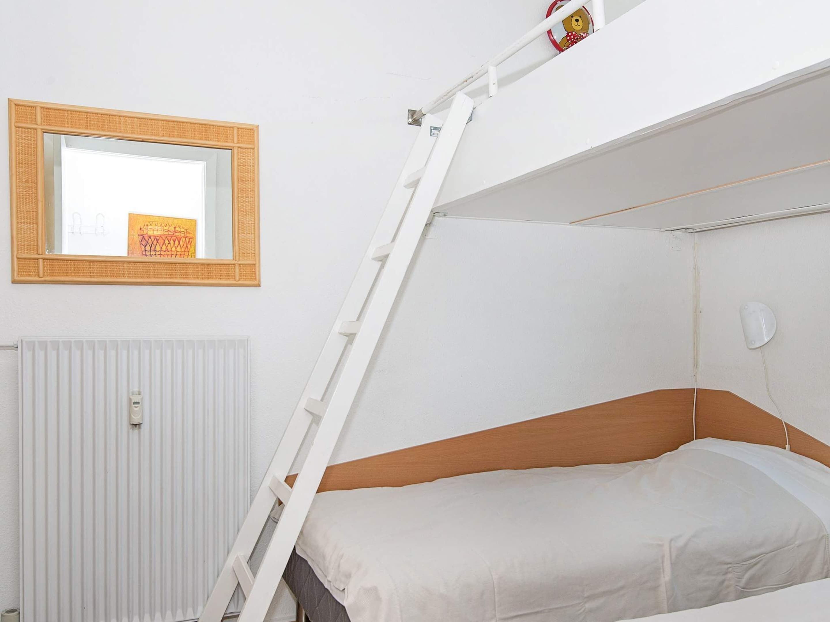A bunk bed with a ladder, a white radiator, and a mirror with a picture frame.