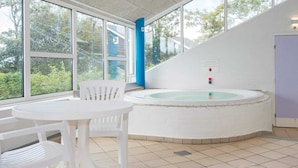 A spa area with a hot tub, white chairs, and large windows offering a view of greenery.