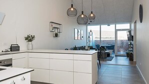 Une cuisine moderne dotée d’un îlot central, de luminaires suspendus et donnant sur un espace patio.