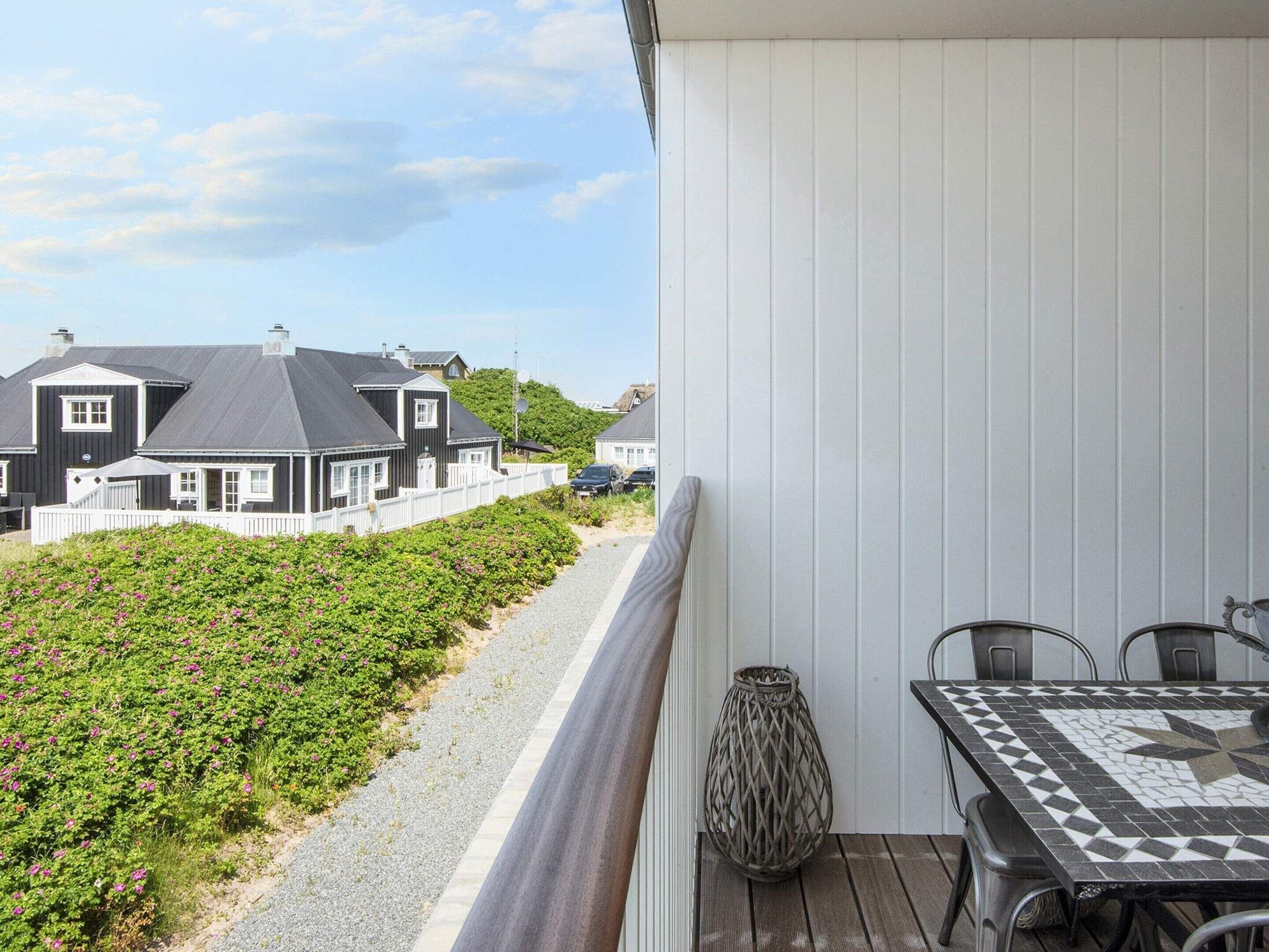Un balcon donnant sur des maisons, un chemin de gravier et une table avec des chaises.