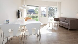 Ein modernes Wohnzimmer mit einem weißen Sofa, einem Esstisch mit Stühlen und einem an der Wand befestigten Fernseher.