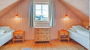 Un dormitorio acogedor en el ático con paredes de madera, un ventanal con cortinas, dos mesitas de noche con lámparas y una cama.