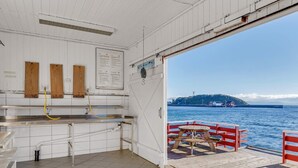 Una cocina pequeña y limpia, con encimeras de acero inoxidable, suelo de baldosas y vista al mar y una isla lejana a través de una puerta abierta.