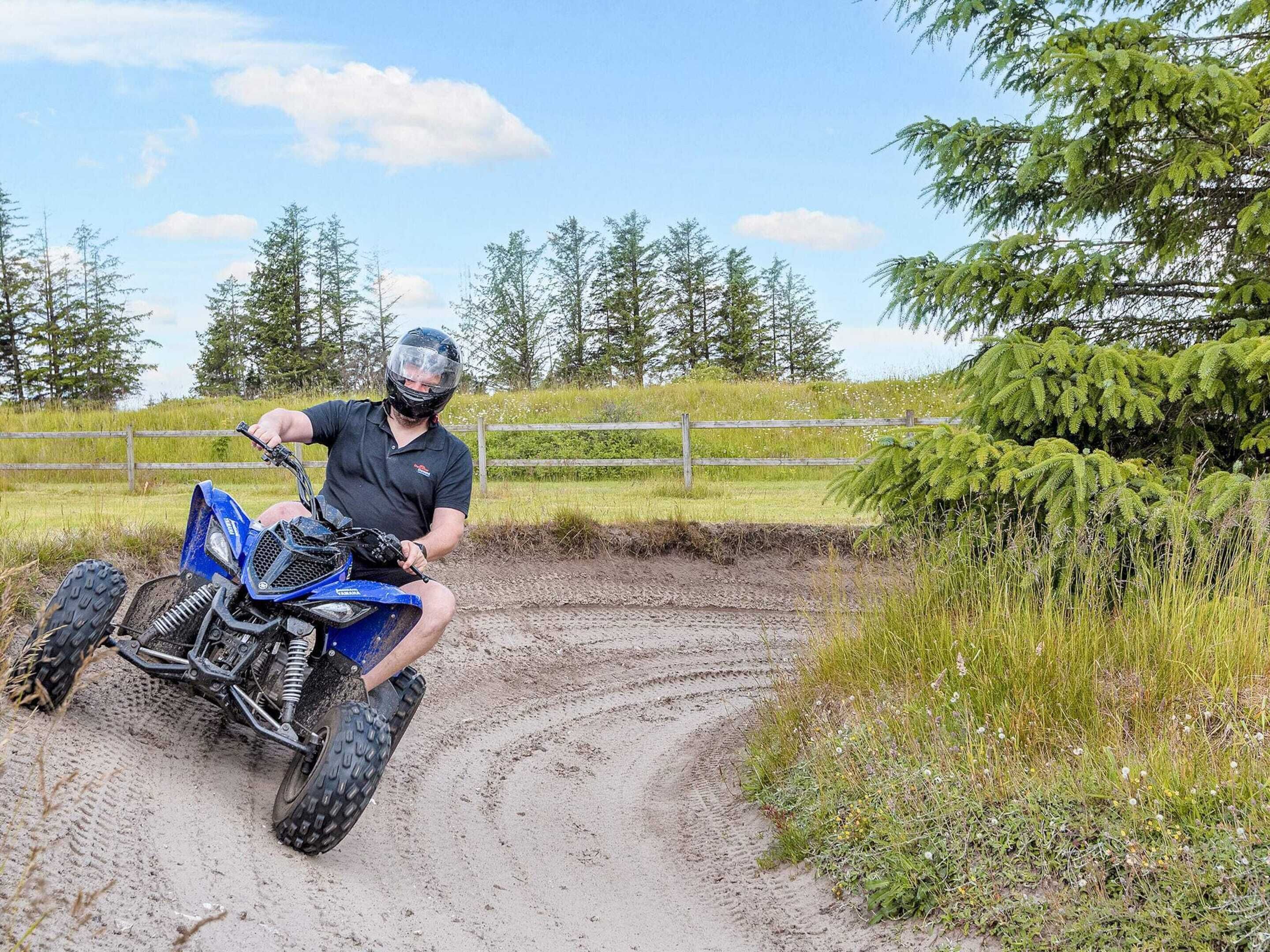 Una persona guida un quad blu su un sentiero sterrato, circondato da vegetazione e alberi.