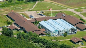 An aerial view of a building complex with multiple structures, including a large glass-enclosed area, parking lots, and surrounding greenery.