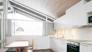 A modern kitchen with white cabinets, a built-in oven, and a dining area with a table and chairs.