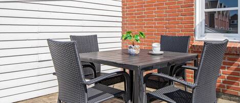 An outdoor patio with a table and four chairs, a potted plant, and a window with a view of a street.