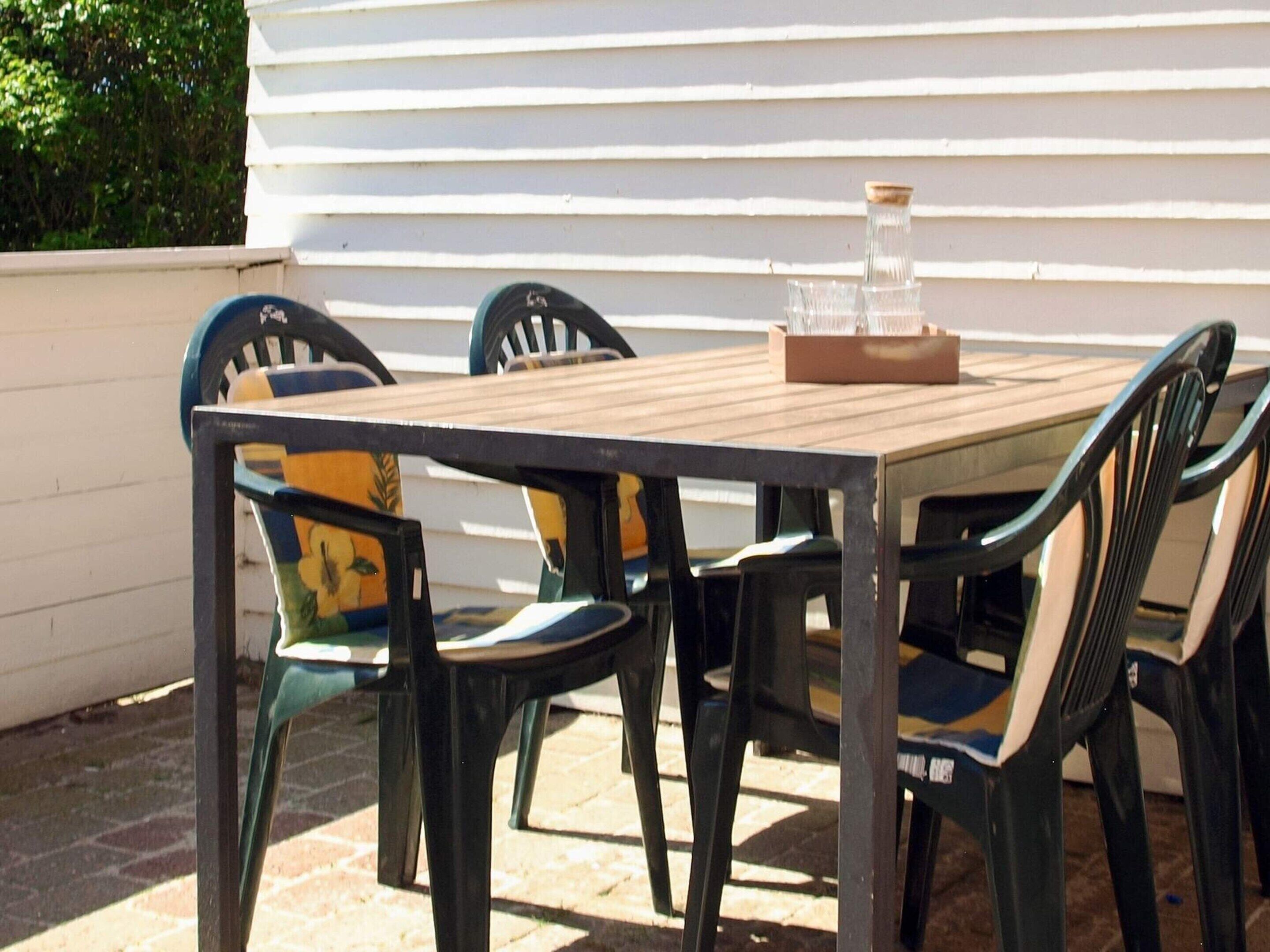 A wooden table with chairs, a glass container, and a white wall in the background.